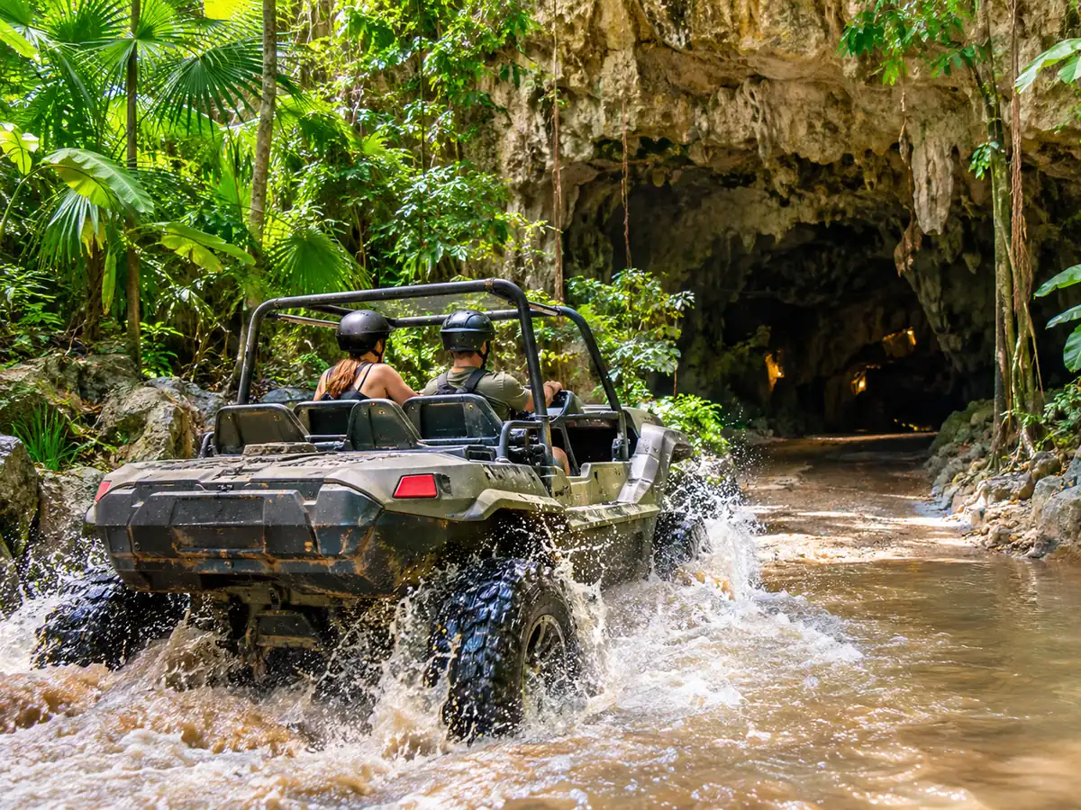 Amphibious vehicle splashing through a jungle pool near a cave entrance