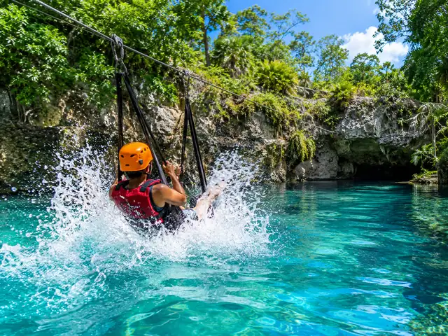 Rider on a hammock zipline splashing into a turquoise cenote
