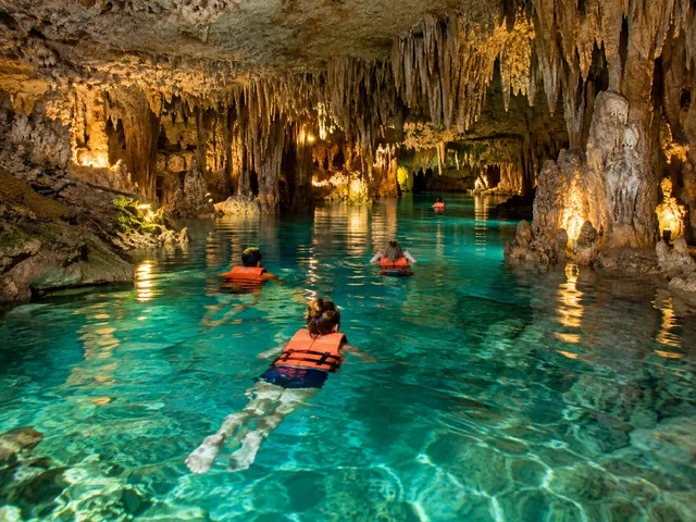 Swimmers in life jackets in a clear underground river among stalactites